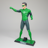 A full-body Green Lantern statue of the character in a dynamic pose, standing on a branded display base in front of a gray metal garage door.