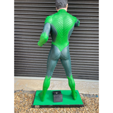 A full-body collectible statue of a superhero shown from the back, wearing a bright green and dark teal suit with a textured, muscular design, standing on a green base in front of a gray metal shutter.